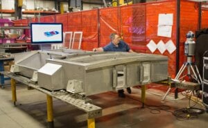 A technician engaged in the process of inspecting a stainless steel fabrication, working on a large, unfinished component with intricate cutouts, showcasing precision metal fabrication quality assurance.